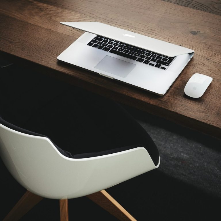 Schlichter Arbeitsplatz mit einem Laptop auf einem Schreibtisch und einem weißen Stuhl.