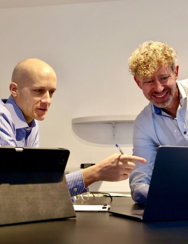 Michael Feiten und Alexander Morgen arbeiten an einem Laptop und diskutieren miteinander.