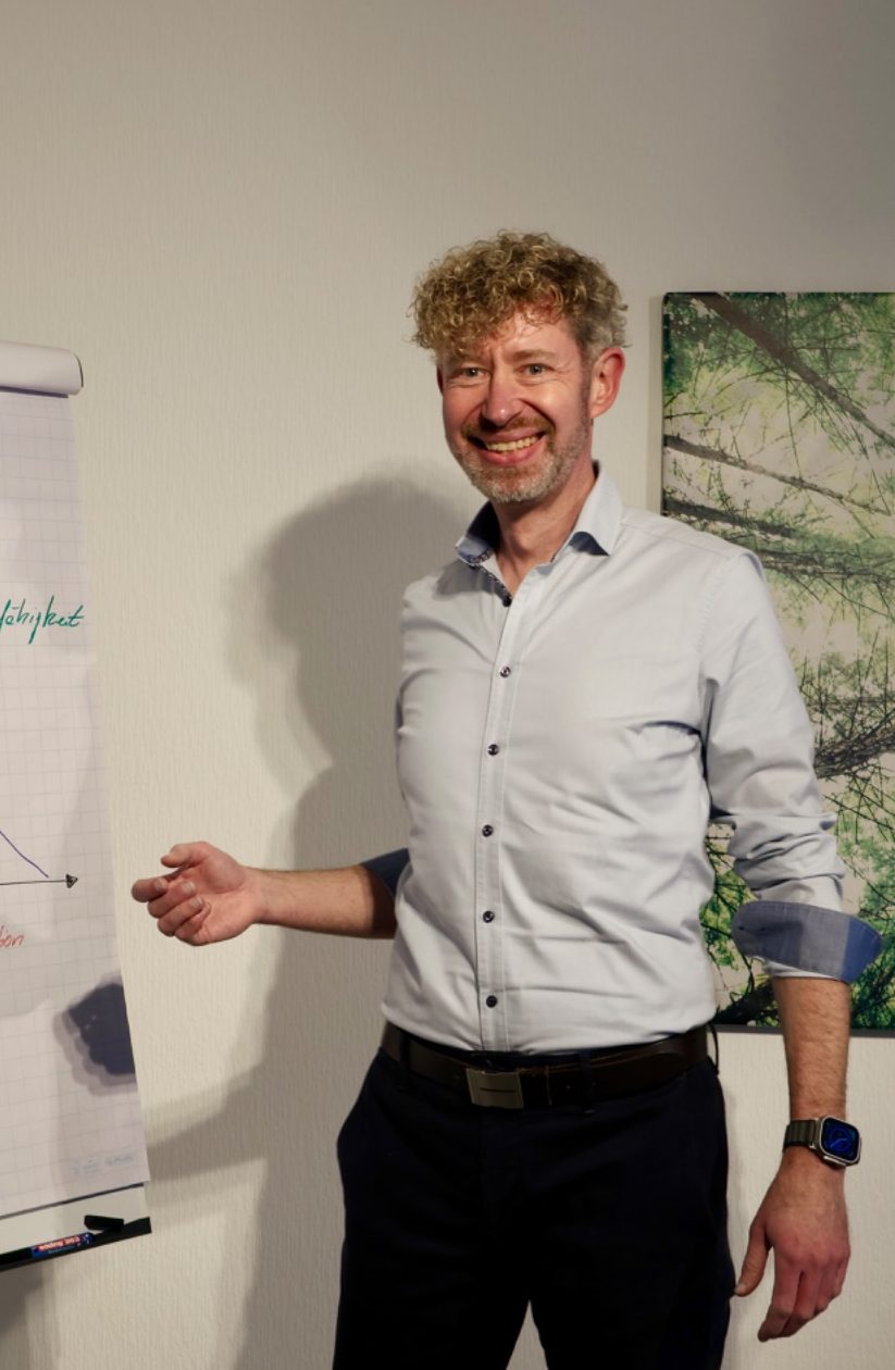 Alexander Morgen steht lächelnd neben einem Flipchart und präsentiert bisherige Ideen.